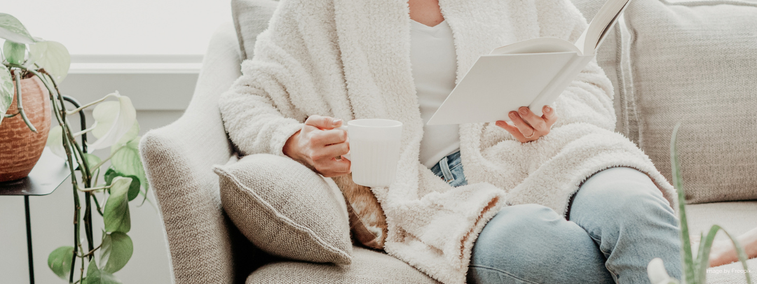 Woman on a couch drinking tea and reading a book.